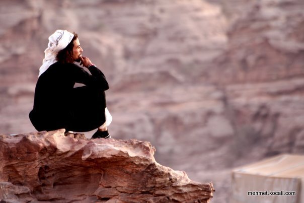 A bedouin sitting on the edge of Jordanian red rocks
