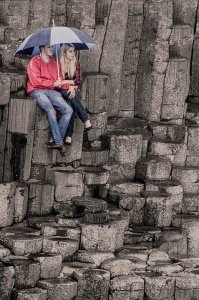 Cute Couple sitting on the columns at Giants Causeway, Northern Ireland, holding an umbrella. A Romantic scene.